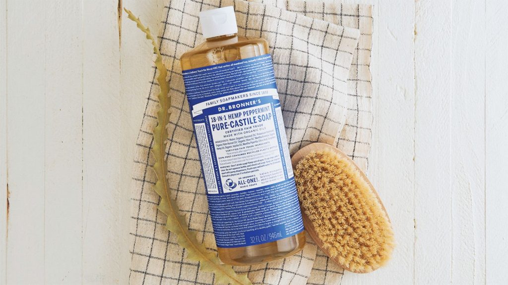 A photo of a bottle of Dr. Bronner’s Pure-Castile Soap next to a bath scrubber.