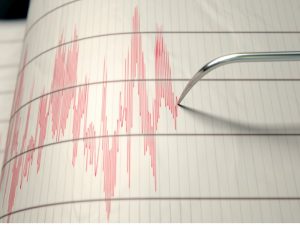 A closeup of a seismograph machine needle drawing a red line on graph paper depicting seismic and earthquake activity - 3D render