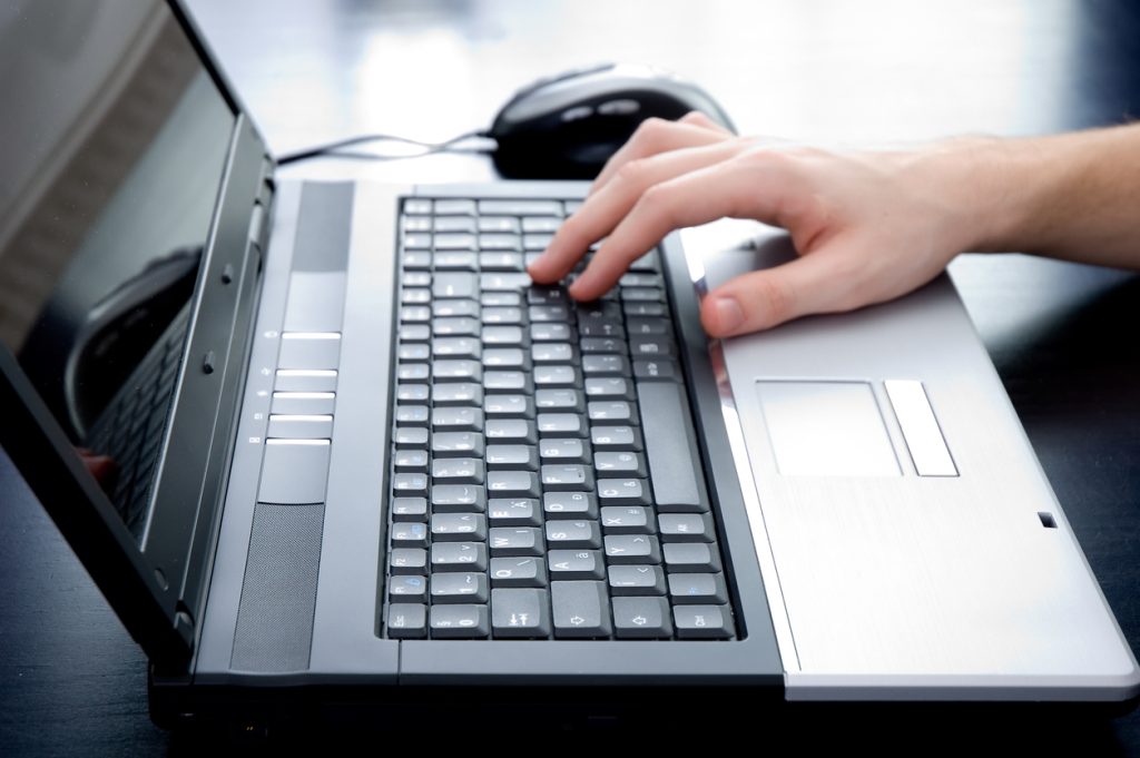 Male hand pushing the enter button on a laptop keyboard. Hand is out of focus