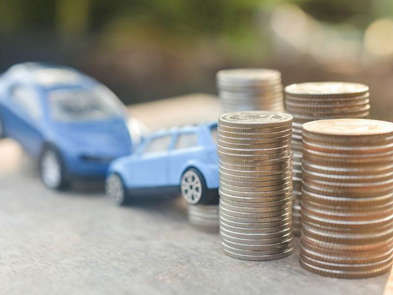 Stacks of coins in the foreground, with blurred blue toy cars in the background.