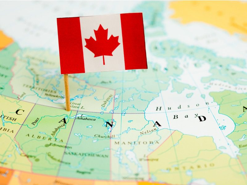 A small Canadian flag is staked out on top of a map of Canada