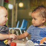 Two toddlers hold hands while playing together at daycare