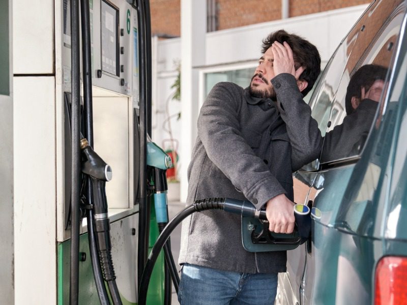 Man at gas pump can't bear to look at the price he'll pay to refuel.