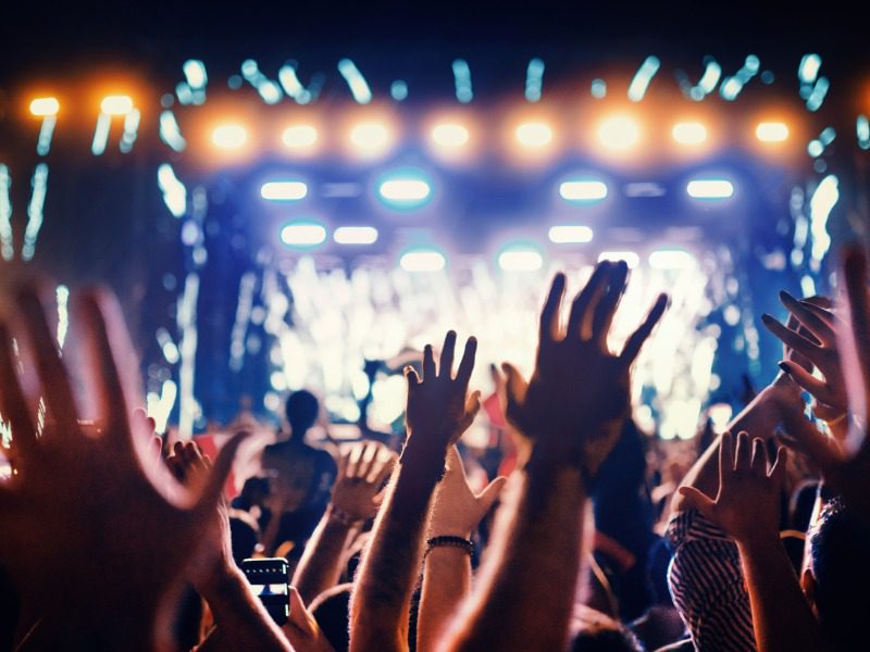 Rear view of large group of people enjoying a concert performance. There are many raised hands in front of the camera.