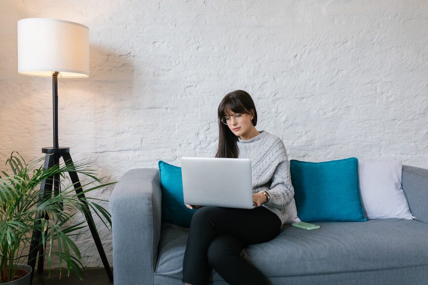 Young girl sitting on a couch in her living room, working on her laptop