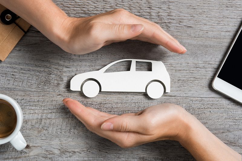 Hands protecting icon of car over wooden table.