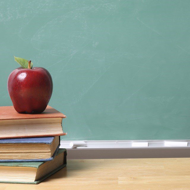 Stack of books and apple on desk in front of blackboard