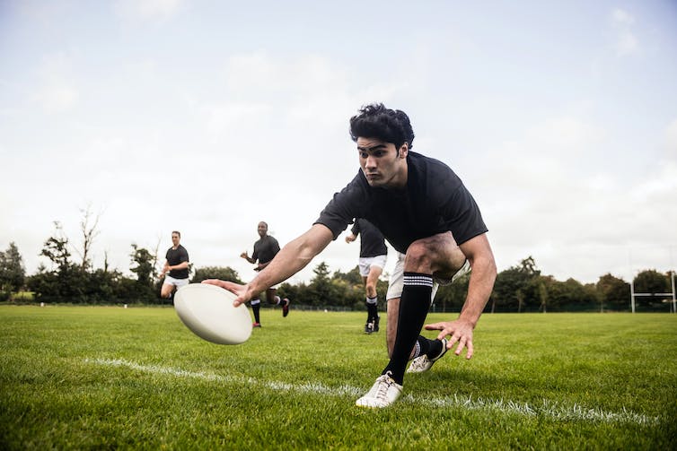 A young boy playing rugby in a black kit.