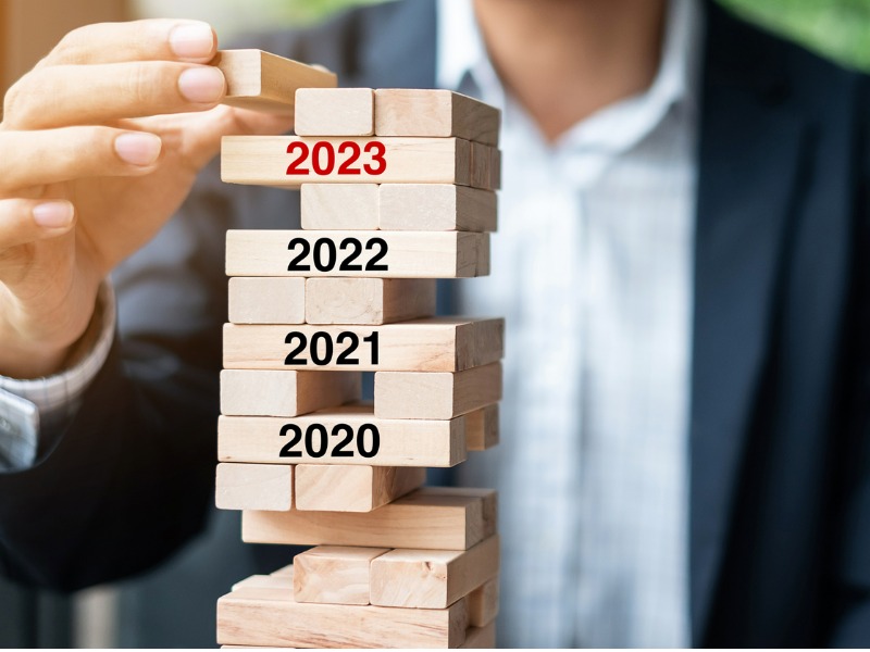 Businessman places wooden block on top of a tower of blocks which have 2023 through to 2020 written on them. hard market stabilized