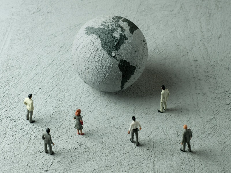 Figurines of six businesspeople examining a concrete globe