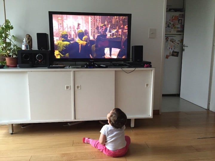 A toddler sits on the floor watching TV in the living room