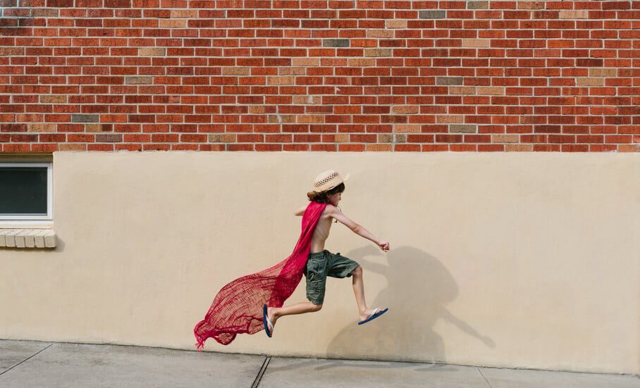 young boy wearing scarf as cape jumps into air, pretending to be superhero