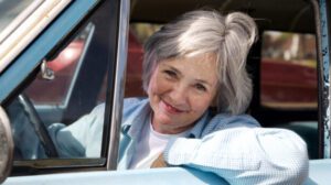 Photography of elderly woman smiling at the camera from the front seat of a truck with hand on wheel to illustrate older drivers