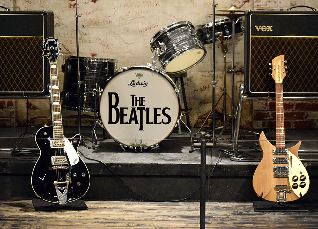 a stage with two guitars, a drum set with the beatles logo and two speakers