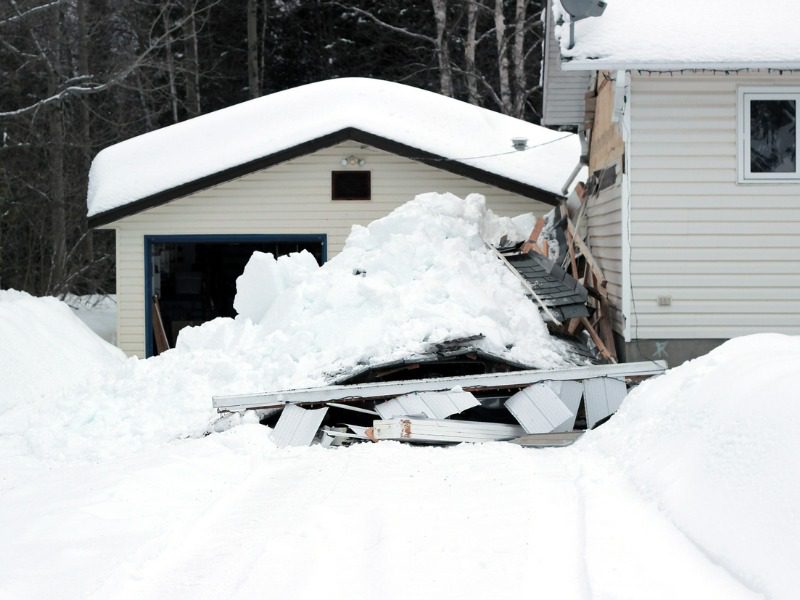 Snow covered carport that has collapsed on top of, and caused damage to two vehicles