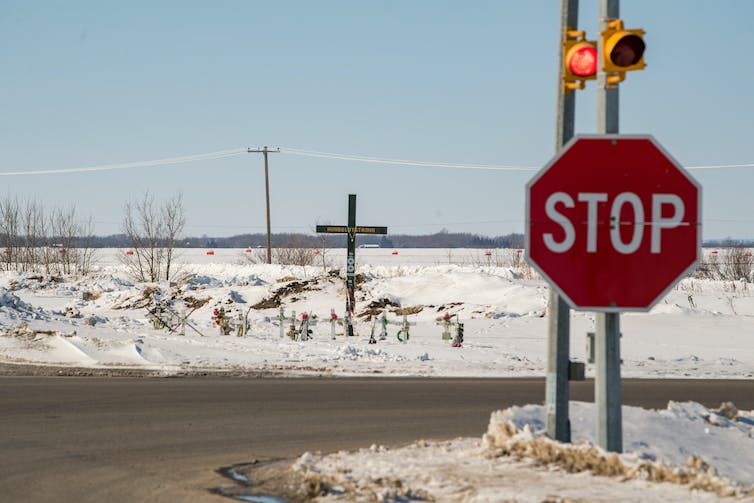 A stop sign at an intersection. A memorial is seen in the background.