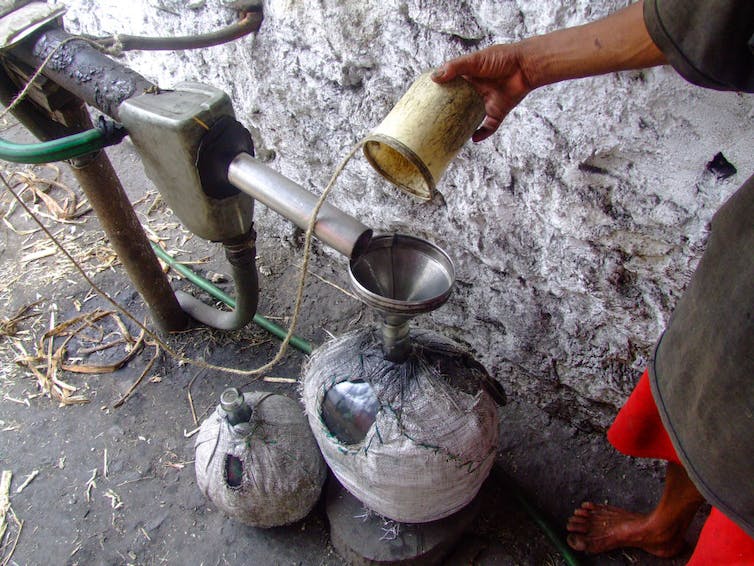 Hand of man holding cup over metal contraption made up of tubes and funnels.