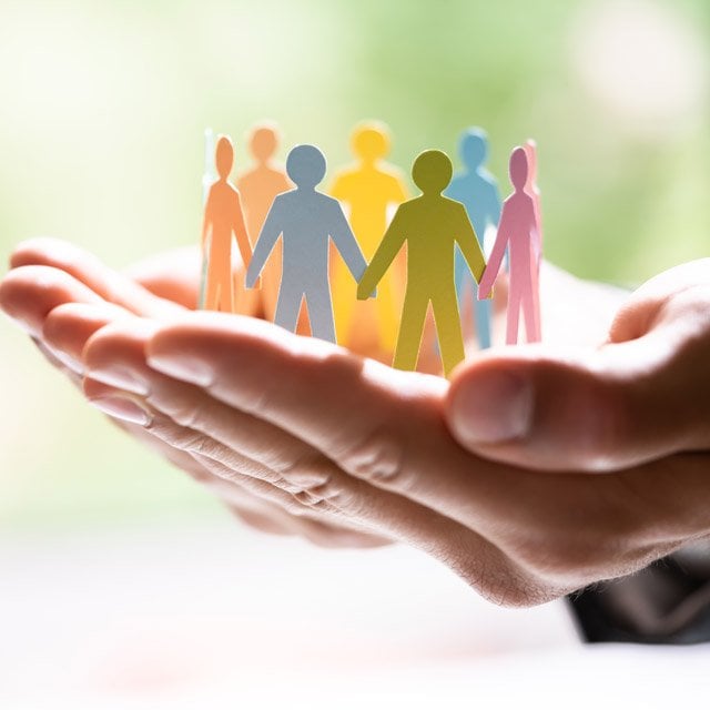 stock image of a person holding out their hand with a circle of multi-colored paper dolls in it