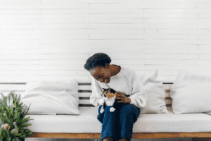 Beautiful young black woman sitting on couch and cuddling her cat