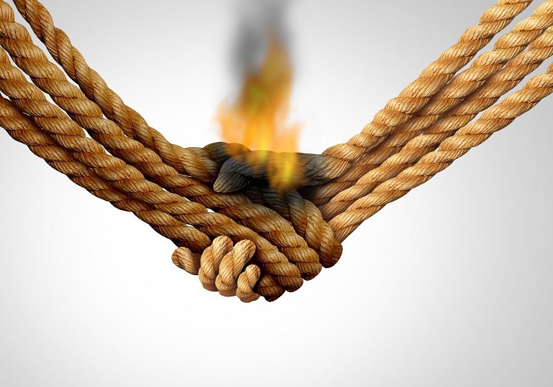 Agreement failure and Business deal fail concept as two hands made of rope in a handshake on fire as a corporate relationship or business crisis and breaking a friendship symbol