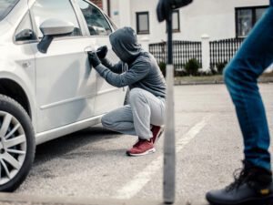Man with a hoodie breaking into a car door