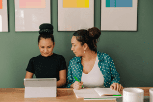 Woman looking at a girl while she works in a computer device sitting on a table at home