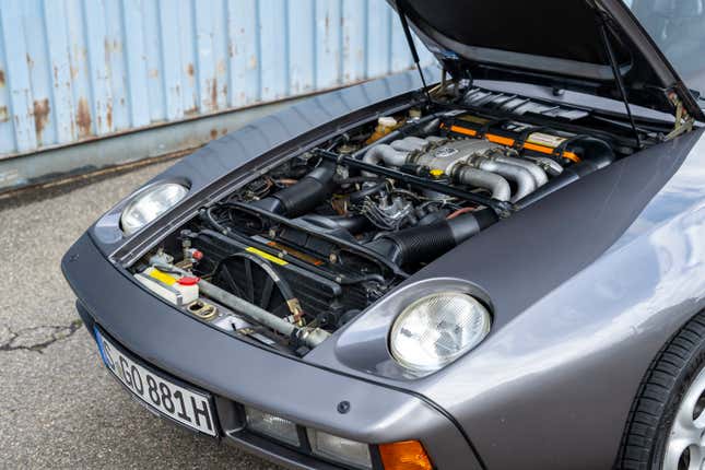 A 1981 Porsche 928 S is parked with its hood up, exposing its V8 engine