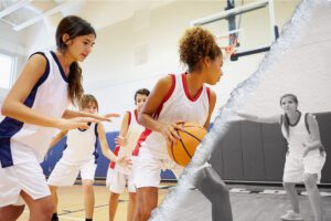 A team of girls play basketball in their school gym.