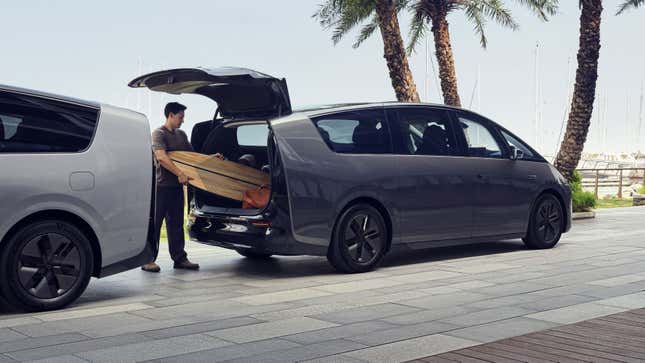 Rear 3/4 view of a man loading a surfboard in the trunk of a Li Mega