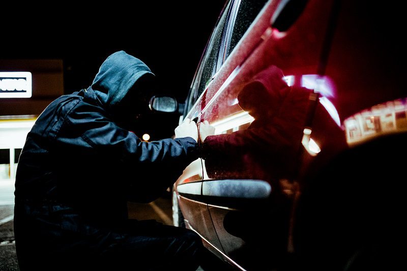 Car thief in action late at night, wearing a black mask on his head