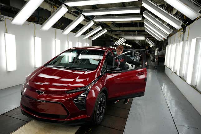 A red Chevy Bolt at the final stages of assembly in a thoroughly lit fluorescent light tunnel at the factory.