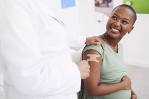 A pregnant woman smiles, her shoulder bandaged after receiving a vaccine