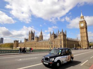 london black cab on the road in front of the houses of parliament with a blue sky and white clouds