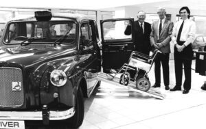 black and white photo of John and Billy Paton standing next to the first wheelchair-accessible FX4 Fairway in the late 1980s