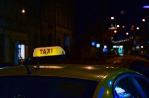 yellow taxi on the street at night surrounded by streetlights with a lit up 'taxi' sign on top of the vehicle