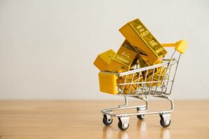 Gold bars in shopping trolley on wooden table with white wall background copy space.