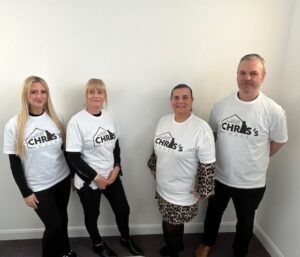 Patons insurance staff stood together in front of a white wall wearing t-shirts with the chris's house charity logo on front