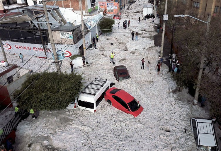 A huge hail storm fills a street with ice up to the hoods of cars in summer.