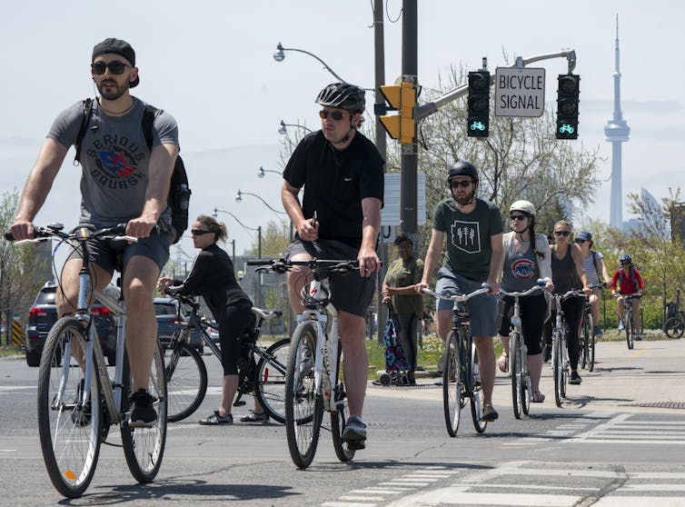 People riding bikes, the CN Tower can be seen behind them in the distance
