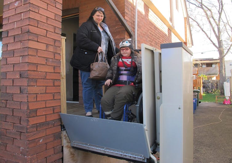 A woman and teenaged girl in a wheelchair using a lift for wheelchair users.